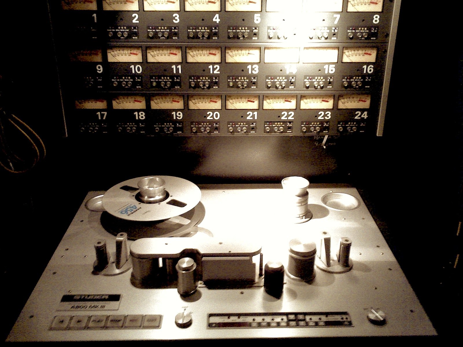 A Studer A800 twenty four track tape machine with a reel loaded and the whole meter bridge lit above it