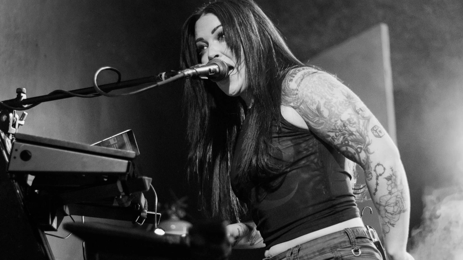 Make Them Suffer keyboardist and vocalist singing into the microphone behind her keyboard rig, tattooed arm in the stage light, black and white, Albury 2025
