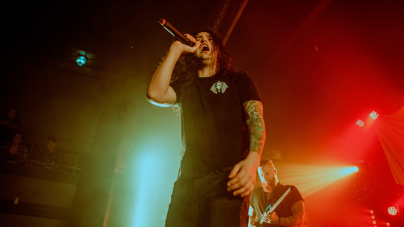 Born of Osiris vocalist at the front of the stage, microphone raised, under green and red stage light, a guitarist playing behind him, Detroit 2019