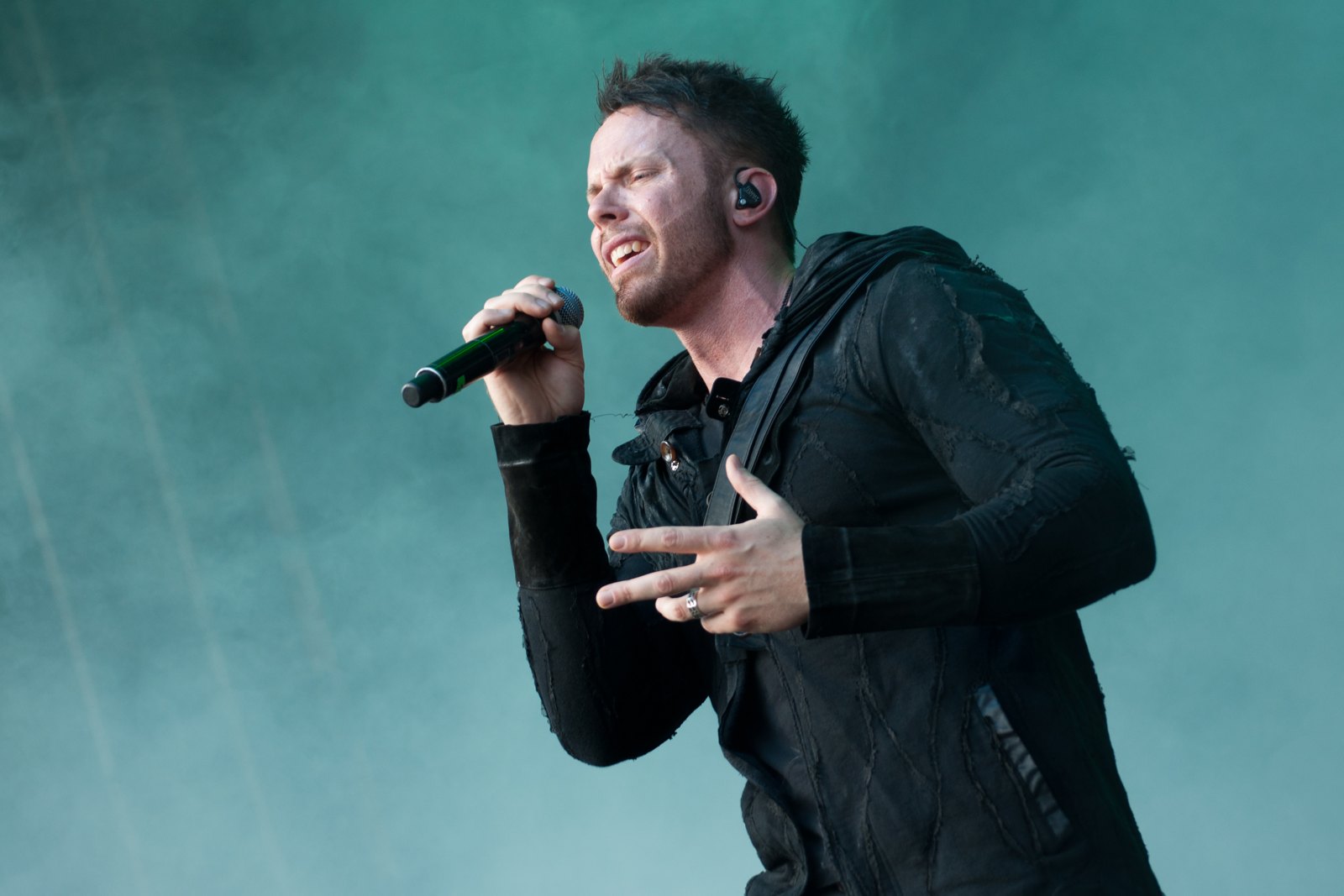 Kamelot singer Tommy Karevik sings into a handheld microphone with one hand raised, in front of stage haze, at the Masters of Rock festival in Vizovice, Czech Republic, 2018.