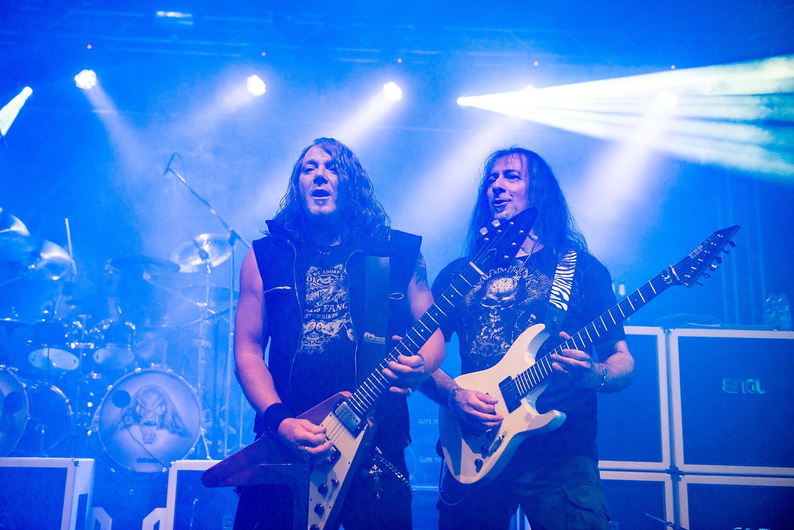 Gamma Ray at Dong Open Air 2015: two guitarists stand side by side at the front of the stage, one with a Flying V and one with a white guitar, in blue stage light with the drum kit behind them.