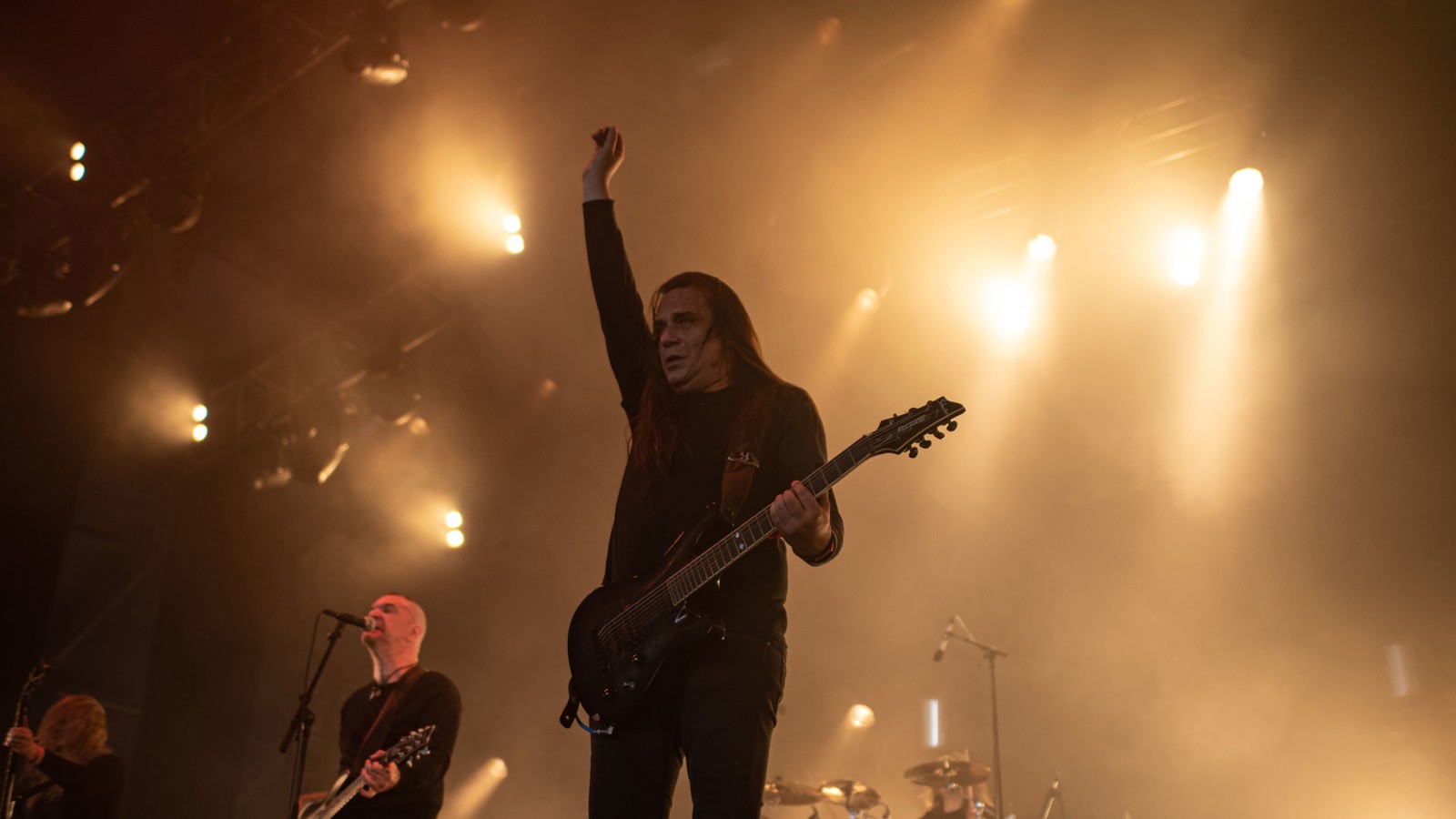 The Ruins of Beverast on a large stage in amber light, a long-haired guitarist raising his fist beside the singer
