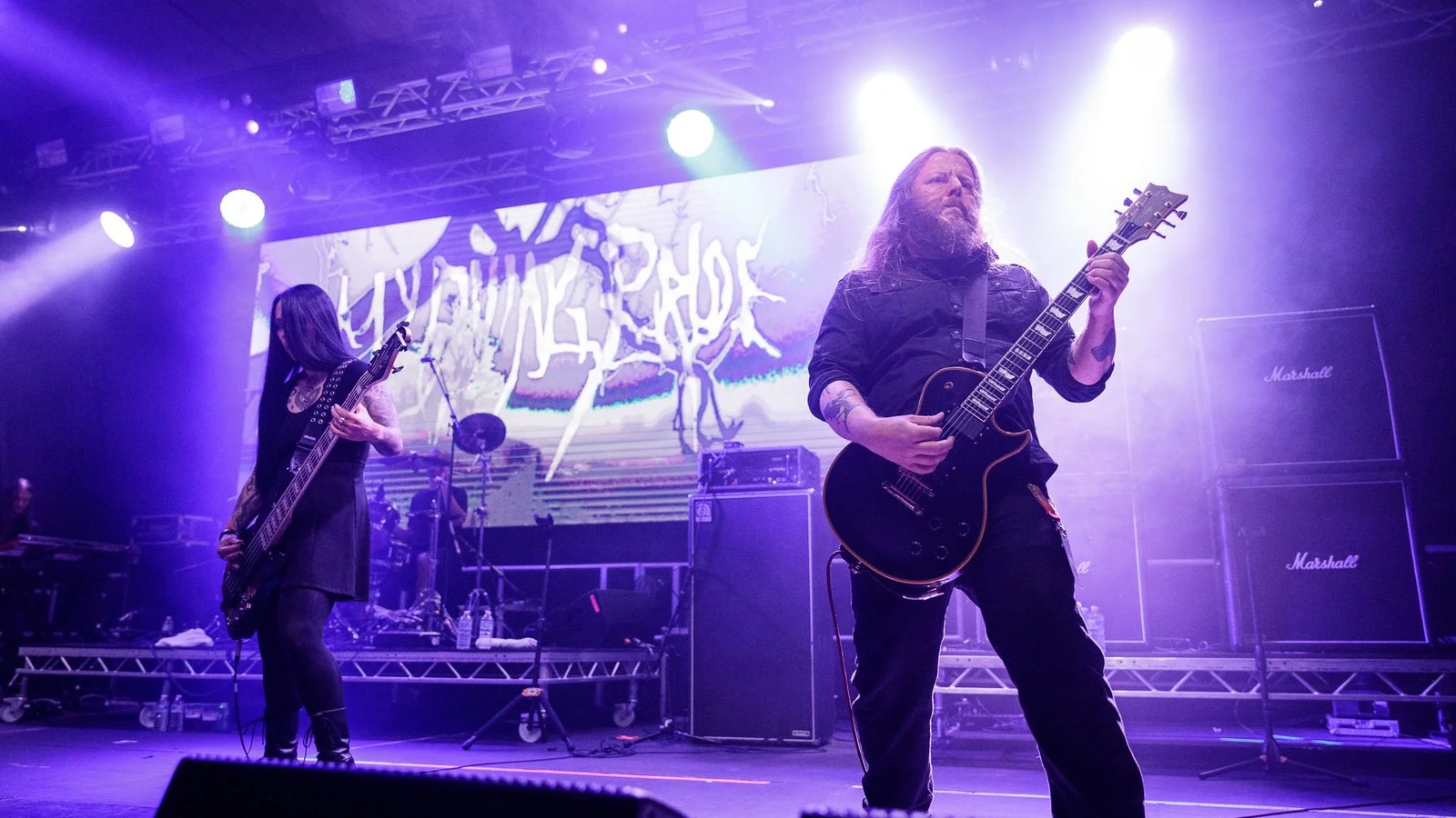 My Dying Bride performing in purple light in front of their backdrop, two guitarists at the front of the stage