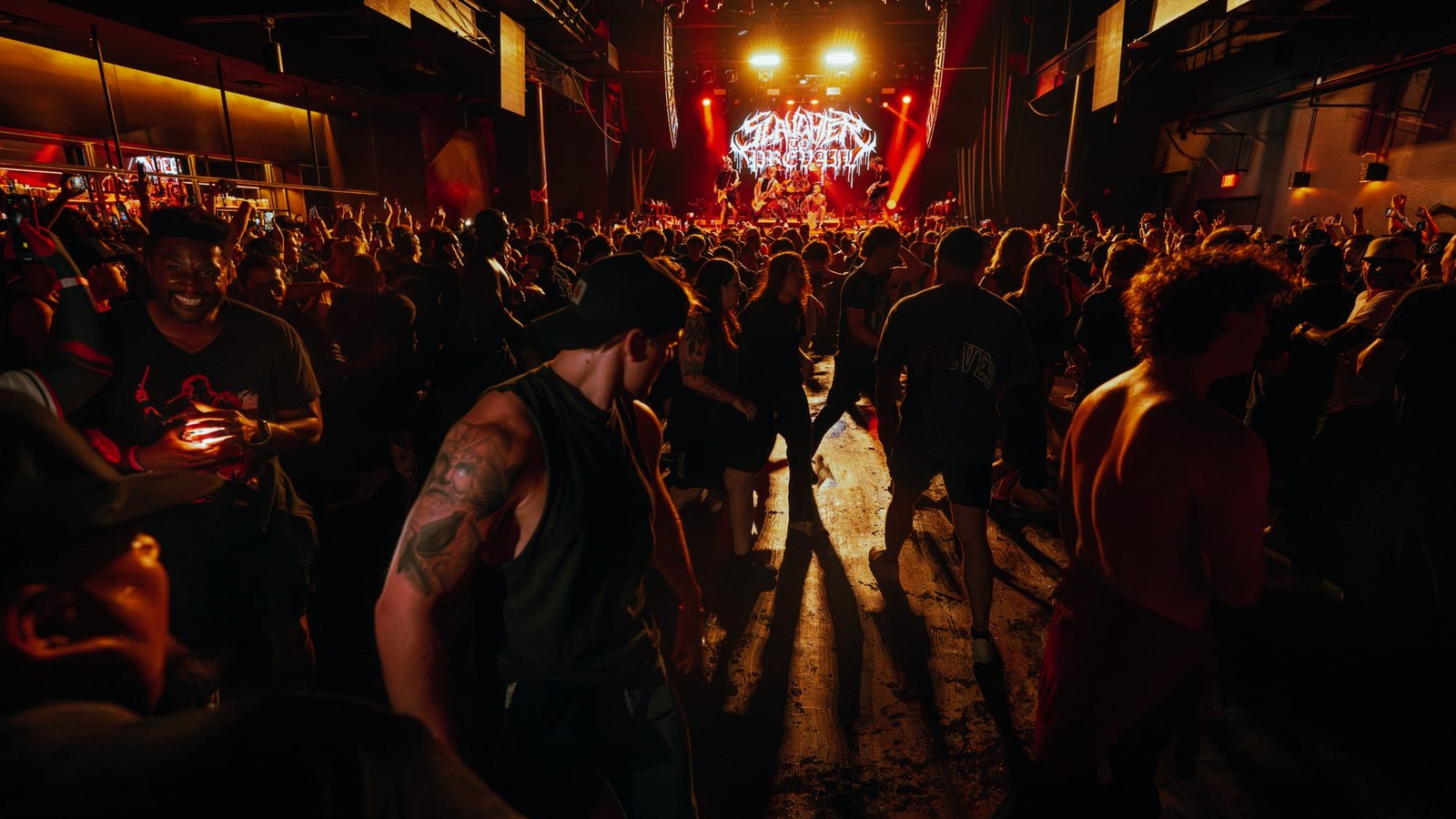 Fans moving through an open pit on the floor of a Dallas venue while Slaughter to Prevail play under their lit logo at the far end of the room, July 2025.