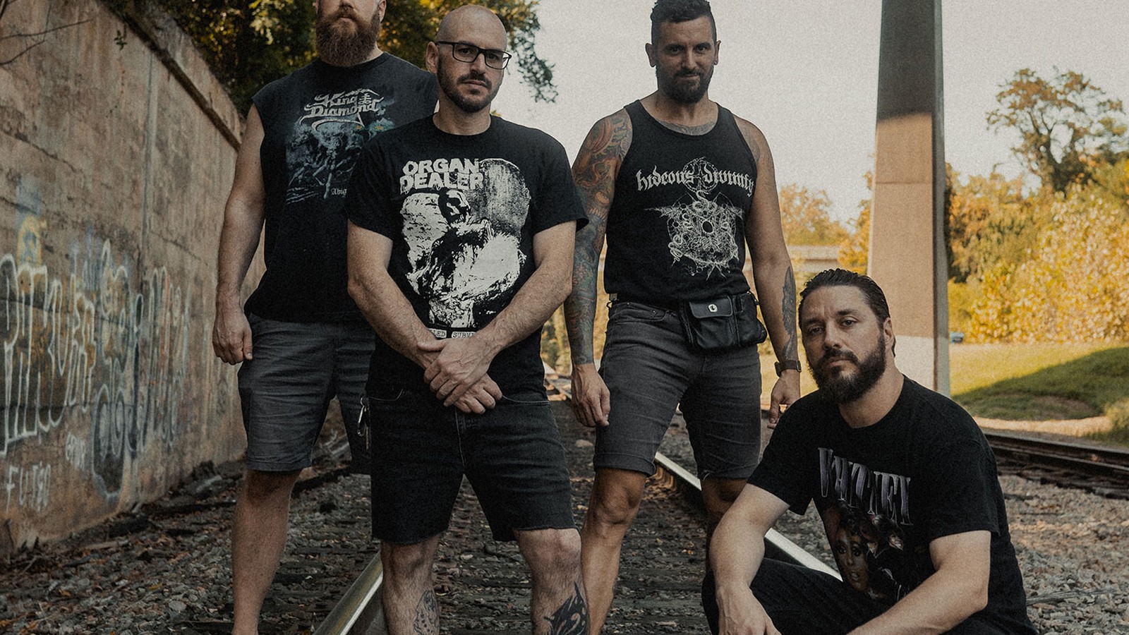 The four members of Job for a Cowboy standing and crouching on a railway track beneath an overpass in autumn light, Moon Healer era press photograph