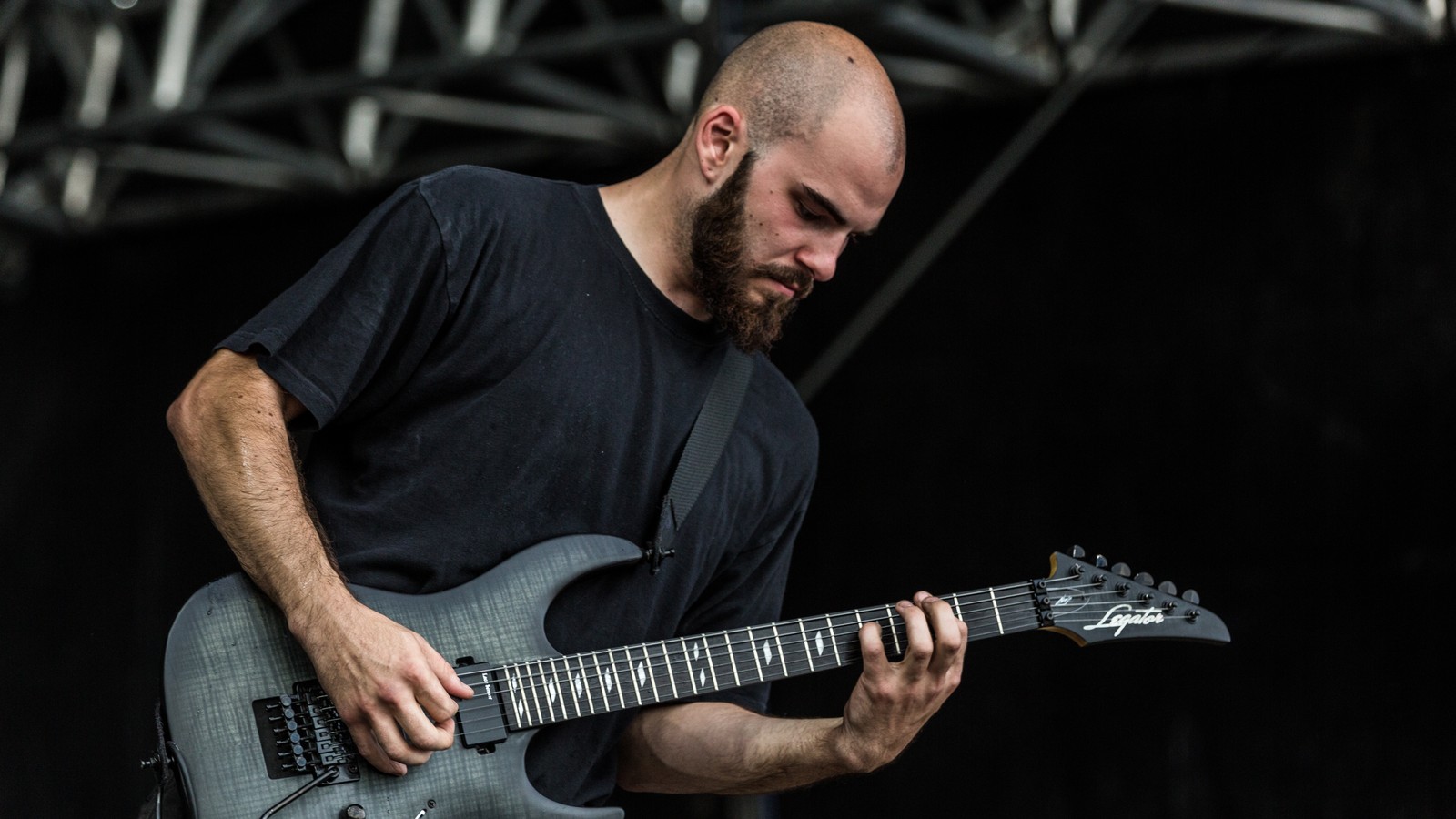 A Suffocation guitarist on the Summer Breeze Open Air stage, head bowed over a grey seven-string, fretting hand high on the neck mid-riff.