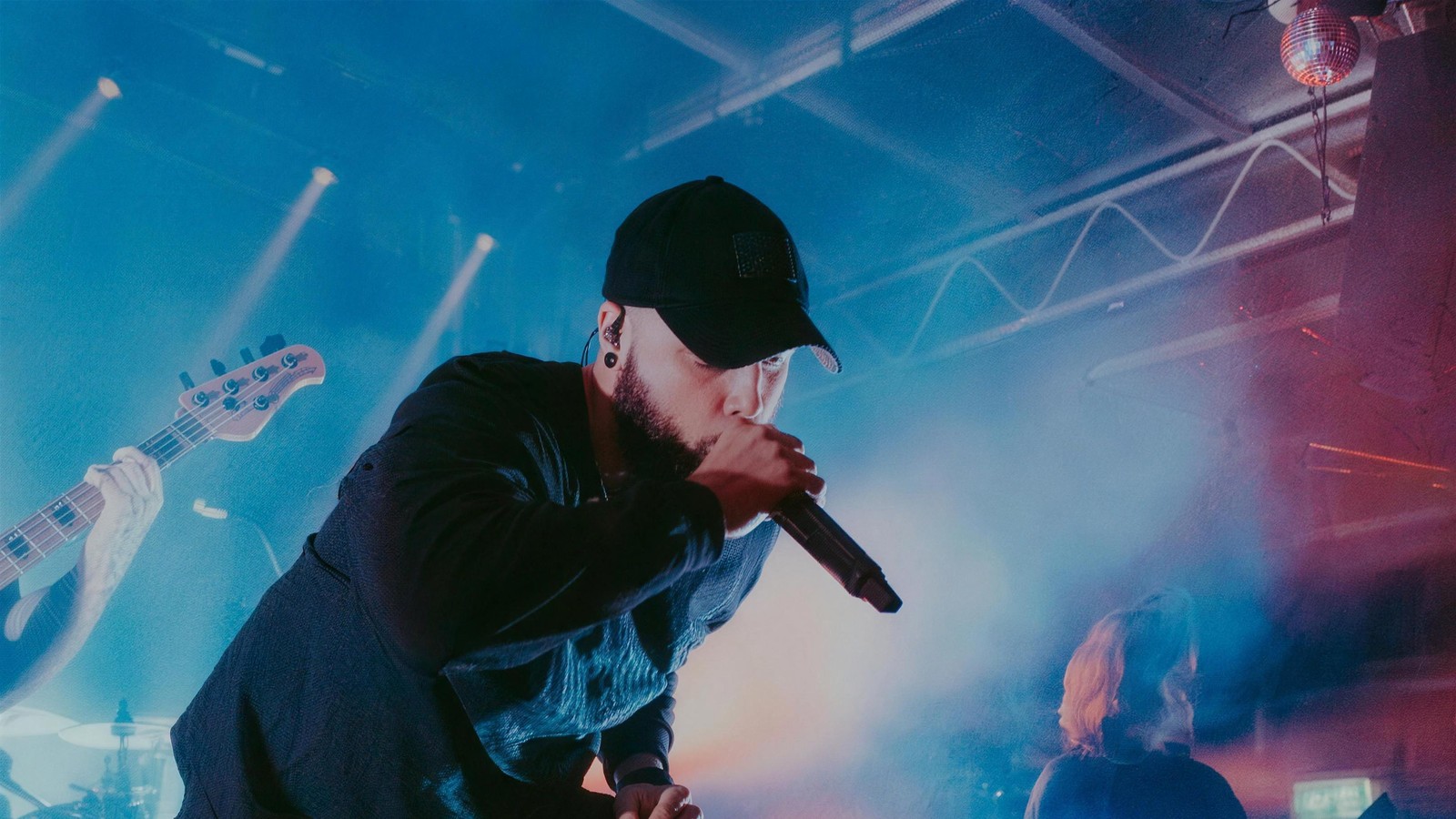 Lorna Shore vocalist Will Ramos leaning back with the microphone raised under red stage light, a guitarist blurred in the foreground and the bassist behind him, Hordern Pavilion, Sydney, 2026