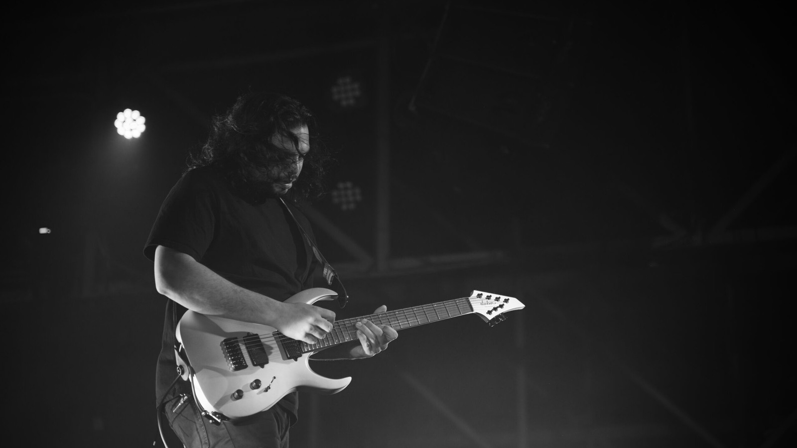 Periphery guitarist playing a seven-string Jackson on stage in a dark hall, fretting hand on the neck, black and white, Nashville, 2024