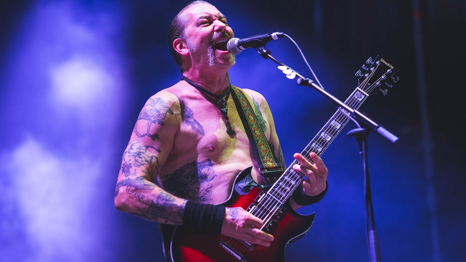 High on Fire singer and guitarist Matt Pike shirtless at the microphone with a red guitar, under blue light
