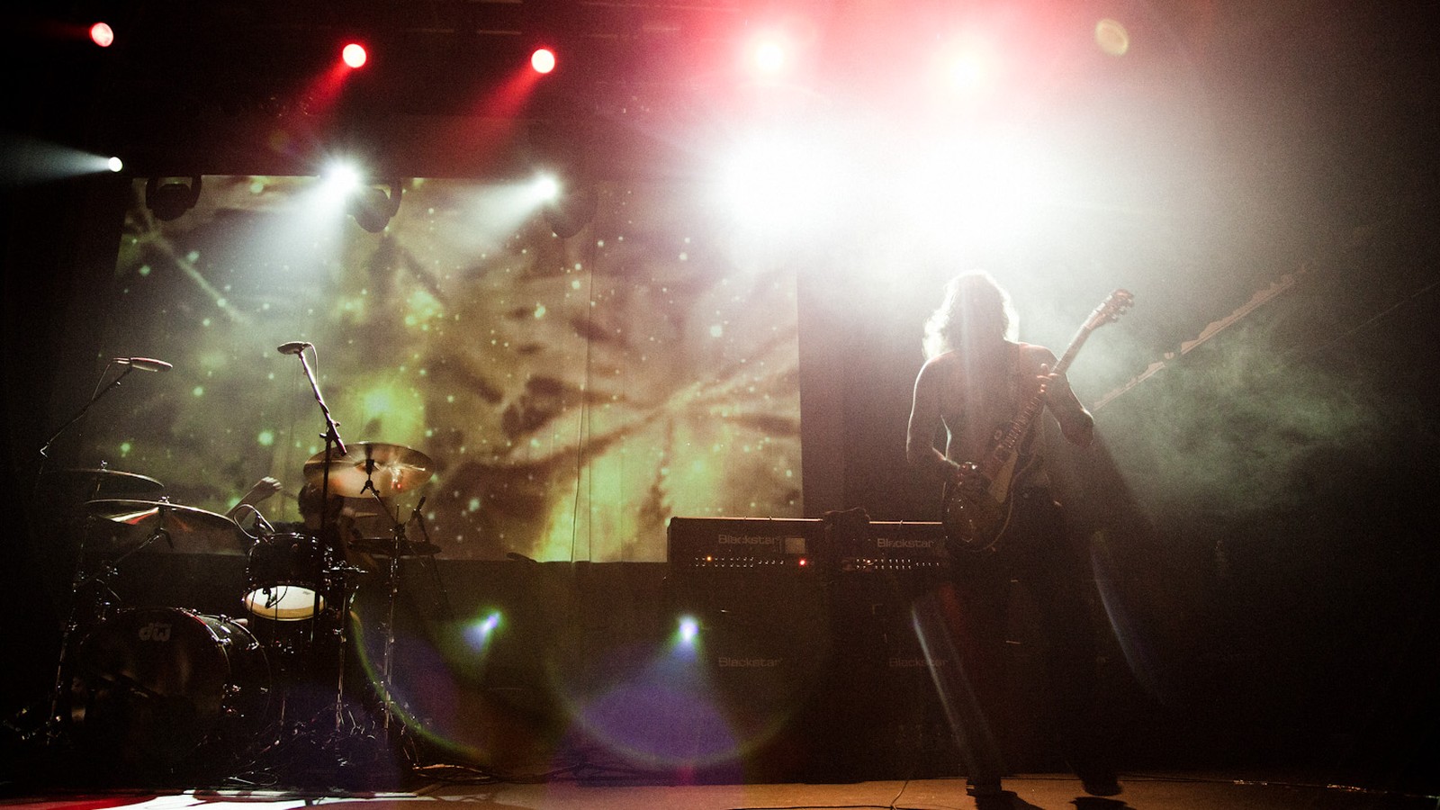 Matt Pike of Sleep backlit on a smoky stage at Terminal 5 in New York, a drum kit and a projection screen beside him