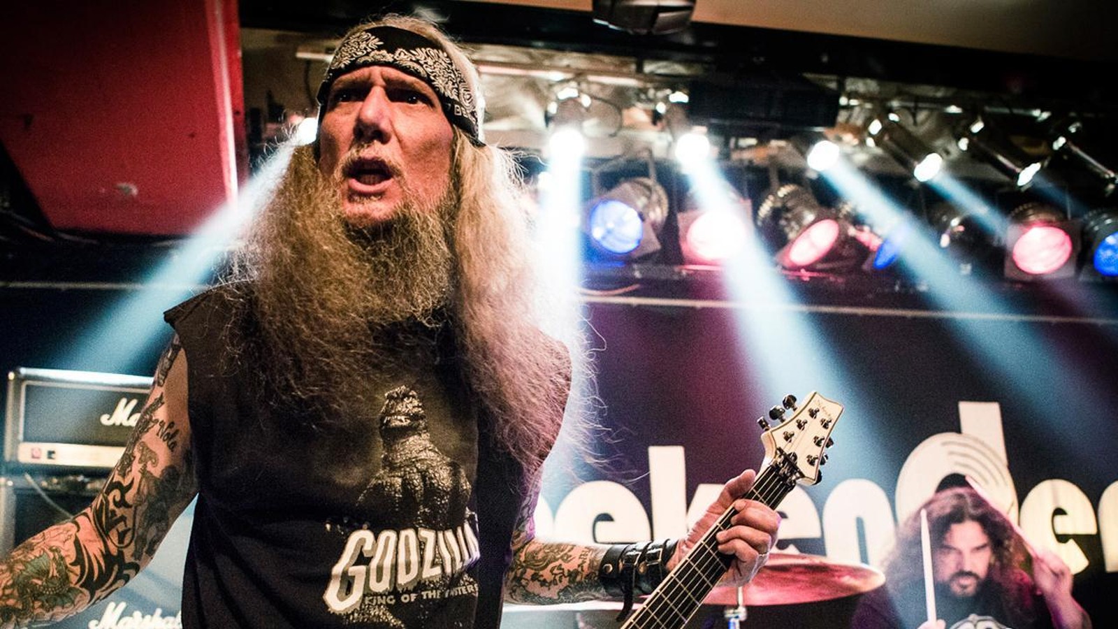 Saint Vitus guitarist Dave Chandler in a bandana playing under white stage lights, the drummer behind him