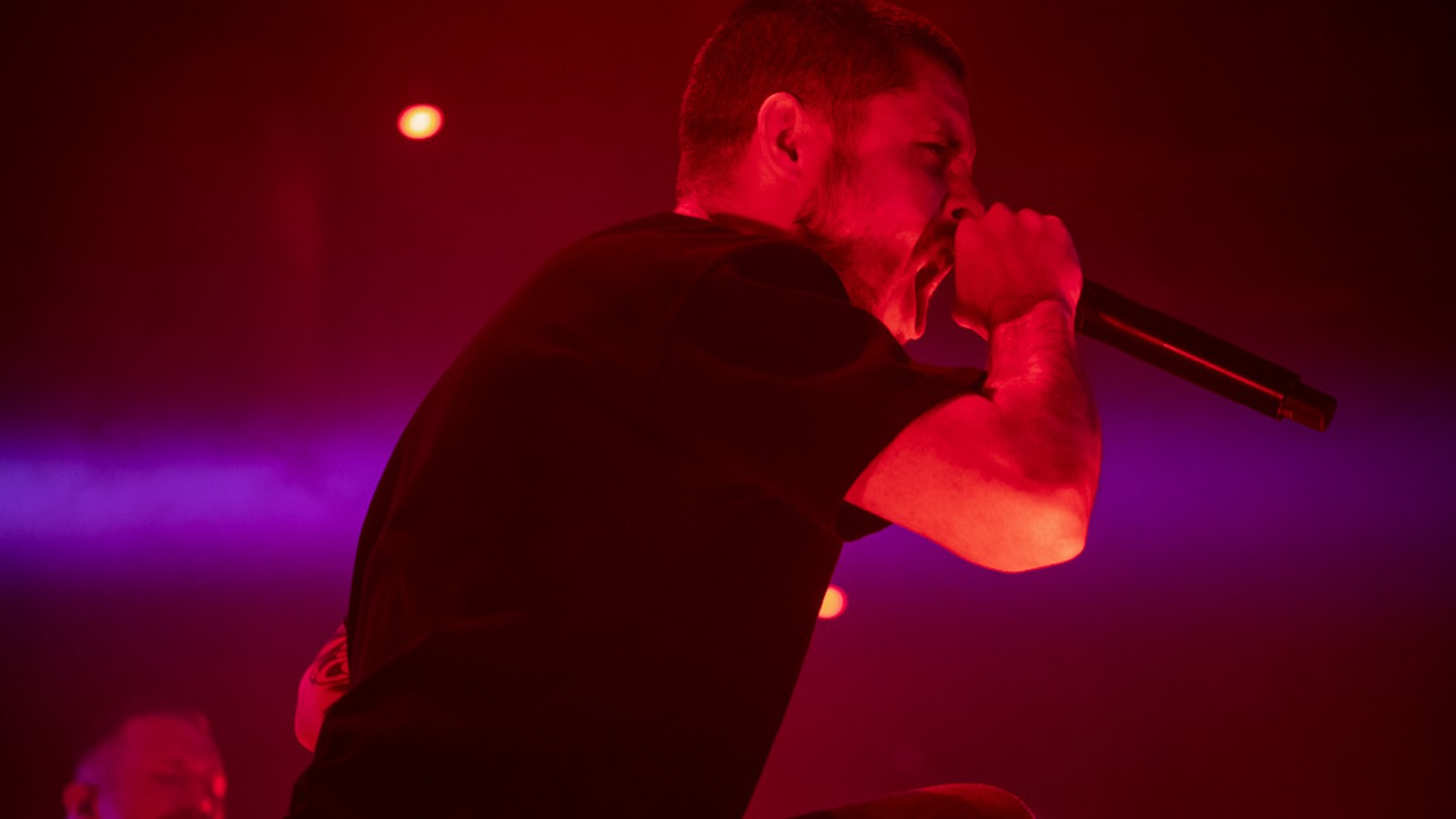 Whitechapel vocalist Phil Bozeman in profile, screaming into the microphone under red and purple stage light at Red Flag in St. Louis, 2023