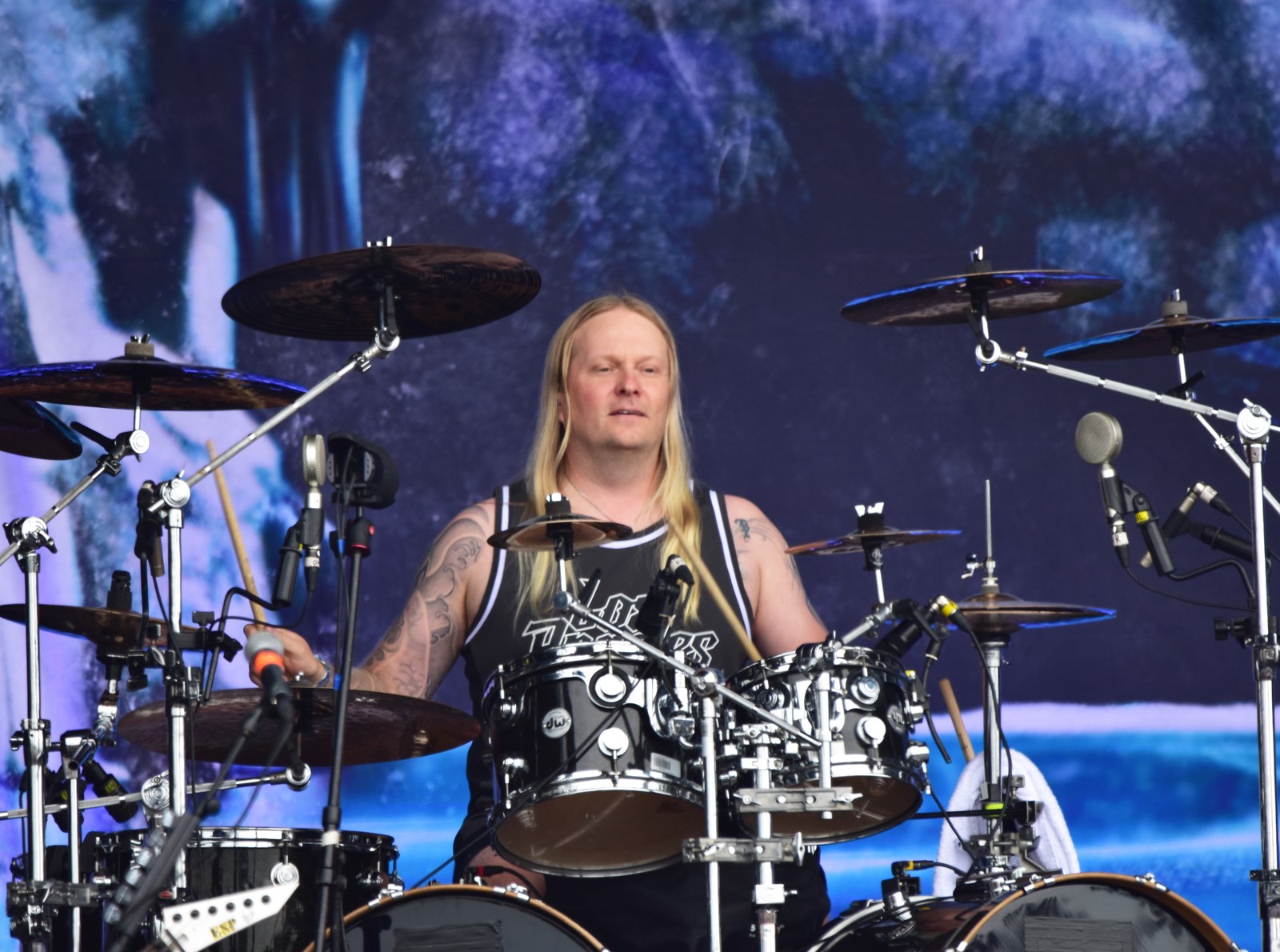 Tommy Portimo of Sonata Arctica at his drum kit on stage at Wacken Open Air 2024, sticks in hand, long fair hair, tattooed arms, surrounded by cymbals and microphones.