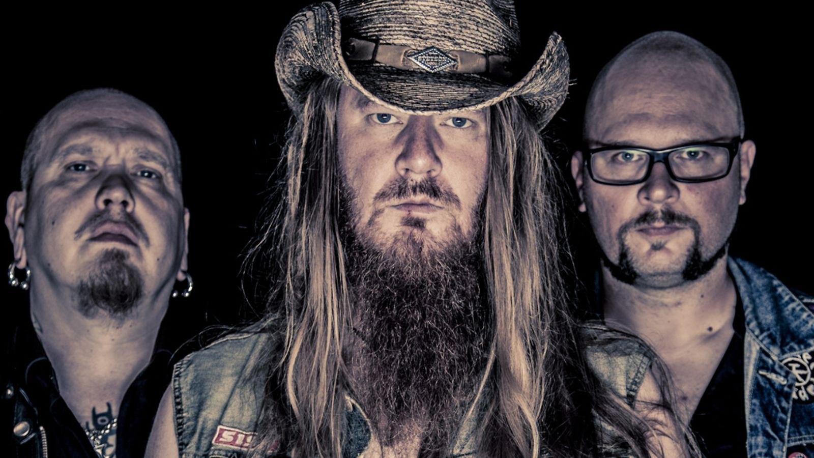 The three members of Kotiteollisuus photographed together against a dark background