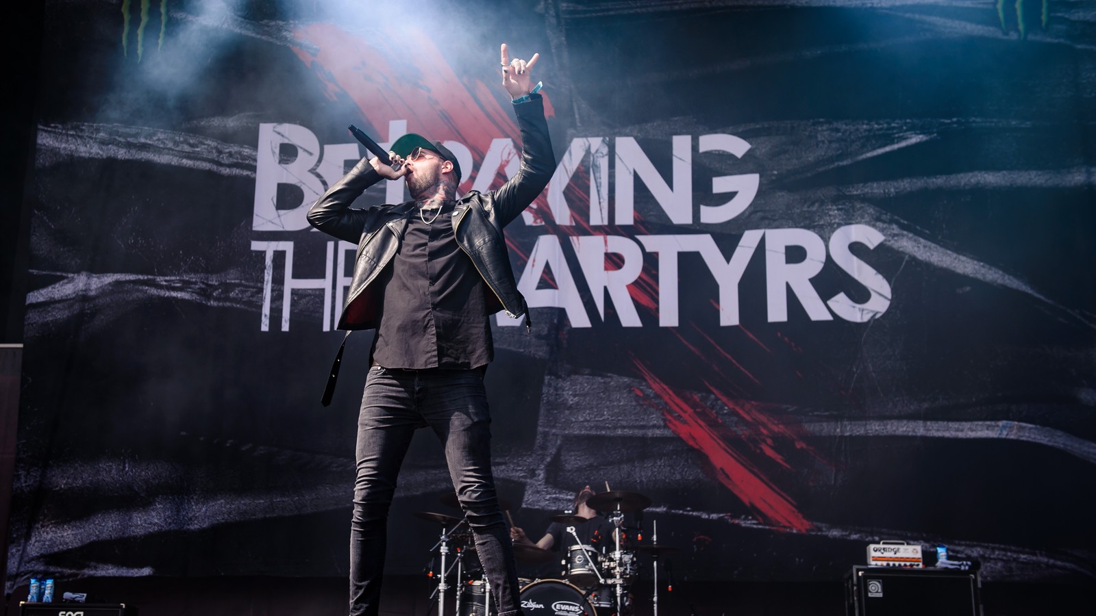 Betraying the Martyrs' vocalist with one arm raised at the front of the stage, the band's logo backdrop and the drummer behind him, Summer Breeze Open Air, Dinkelsbühl, 2018.