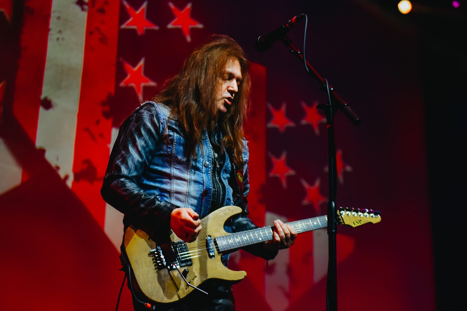 Skid Row guitarist performing live in Detroit, March 2023, red stage light against an American flag backdrop