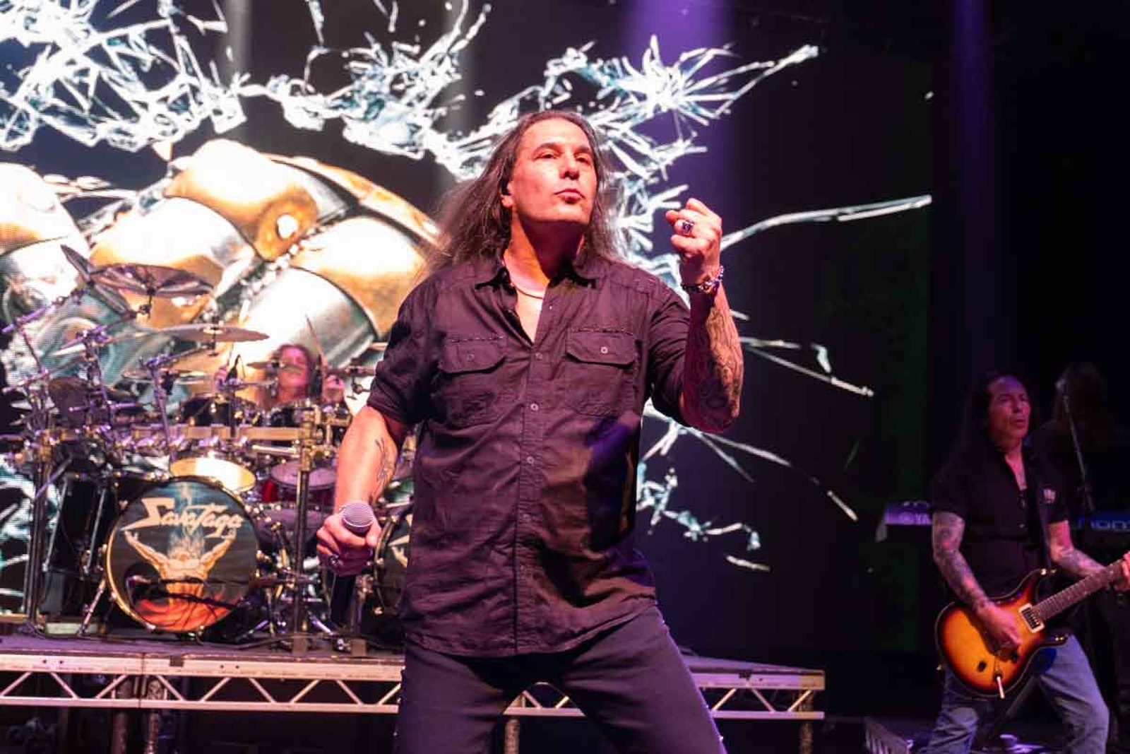 Zak Stevens of Savatage singing at the Shepherds Bush Empire in June 2025, the drum kit carrying the band name behind him