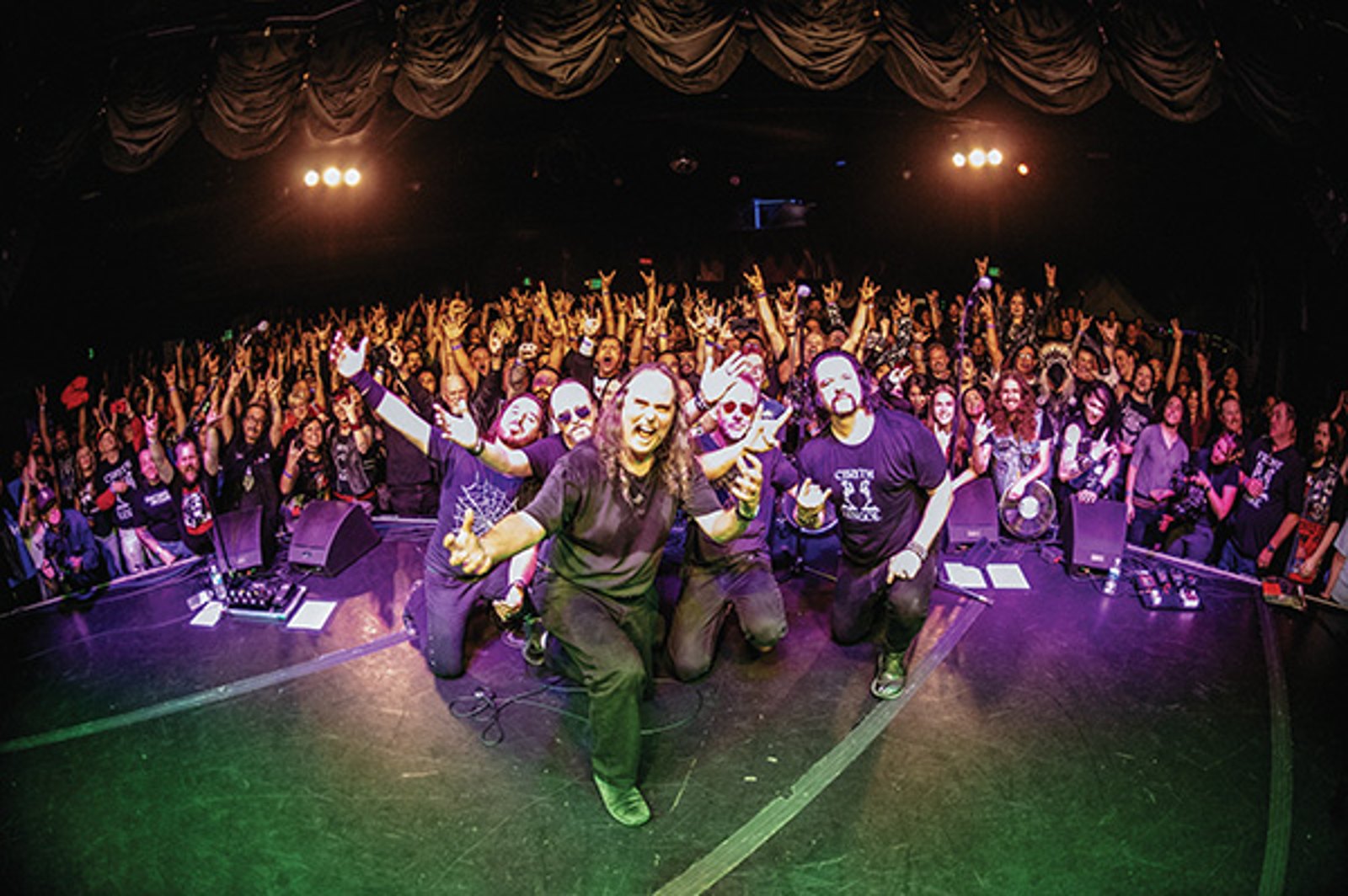 Cirith Ungol kneeling at the front of the stage with their arms raised, the crowd packed behind them