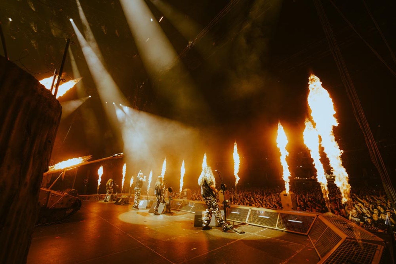 Sabaton performing live at the OVO Hydro in Glasgow, 18 April 2023, band members in camouflage stage fatigues on a war-themed set with a mounted gun barrel, sandbags and flame jets along the barricade