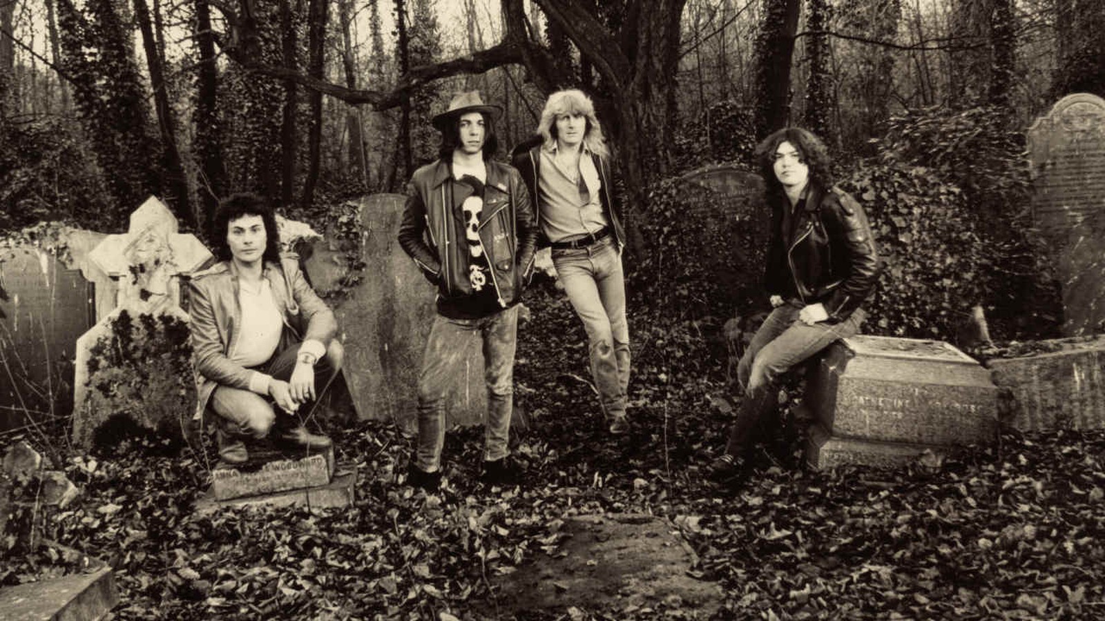 Pagan Altar, four musicians in leather jackets posing among old gravestones and ivy in a churchyard