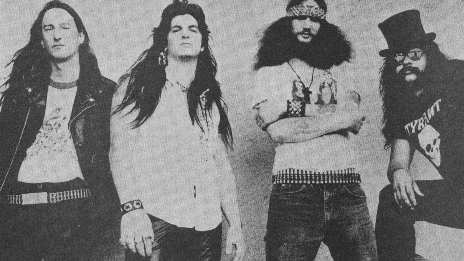 Saint Vitus, four long-haired musicians in bullet belts, a bandana and a top hat, in a black and white 1980s band photograph