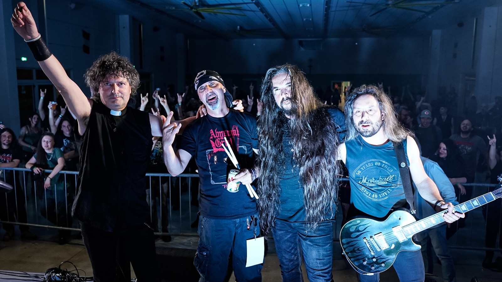 The four members of Lord Vicar posing on stage after their set, the singer in a clerical collar raising his fist, the crowd behind them
