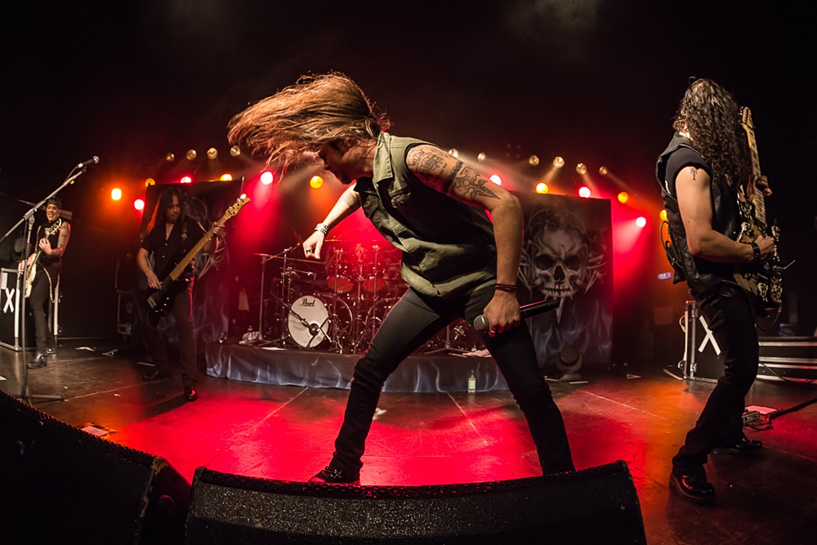 Queensryche performing live at Theaterfabrik in Munich, 25 October 2013, the singer bent forward mid-throw with the band's skull backdrop lit up behind him