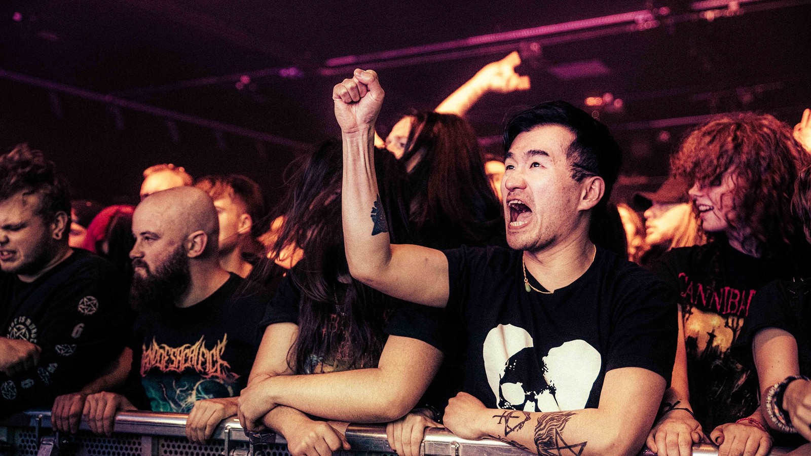 Fans packed against the front barrier at a Thy Art Is Murder show at the Academy in Manchester, one man shouting with a raised fist in the stage lights, 2023