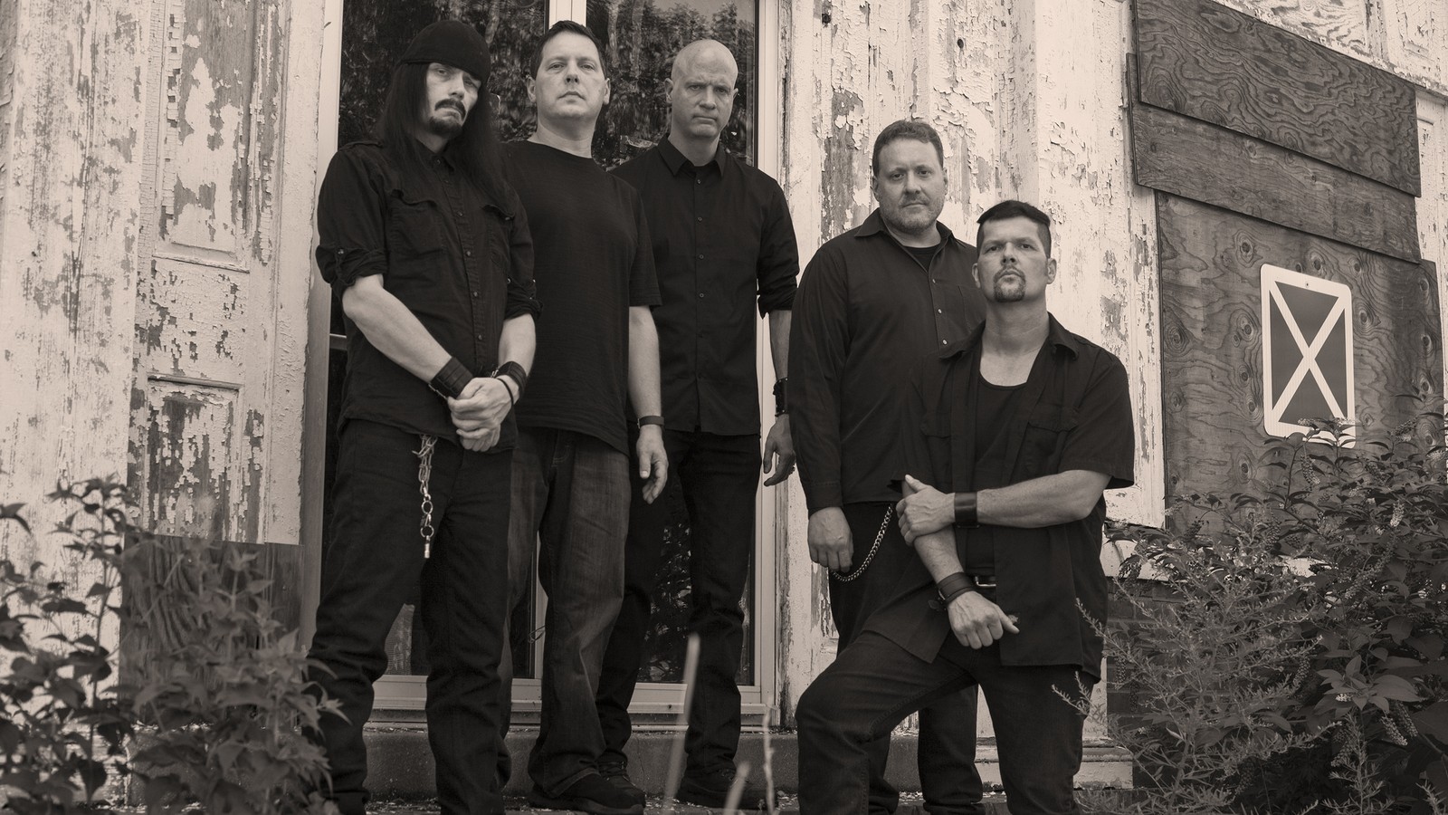 The five members of Evoken in black on the steps of a derelict building with peeling white paint, in sepia