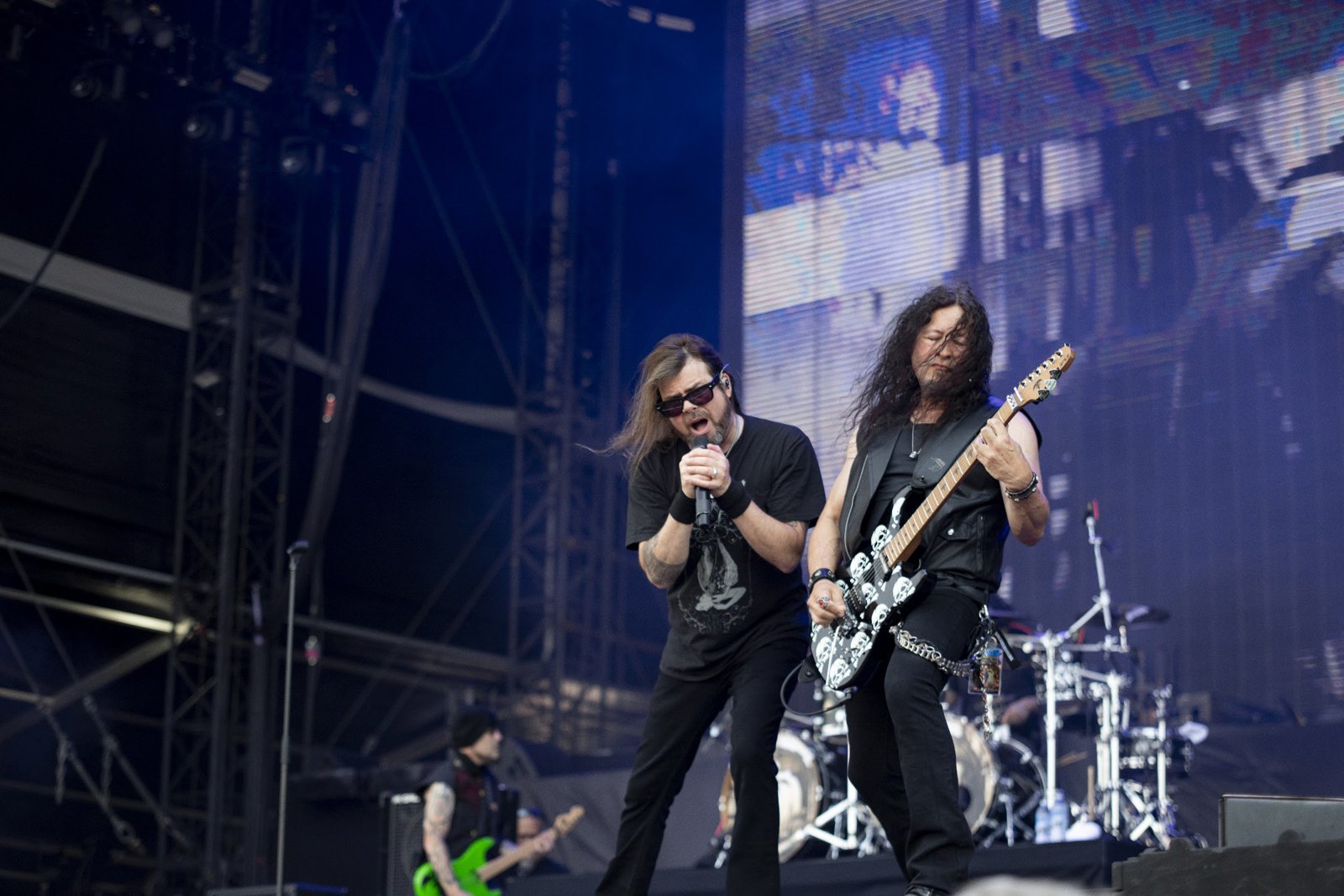 The singer of Queensryche in sunglasses at the microphone and a guitarist beside him on a festival main stage in daylight