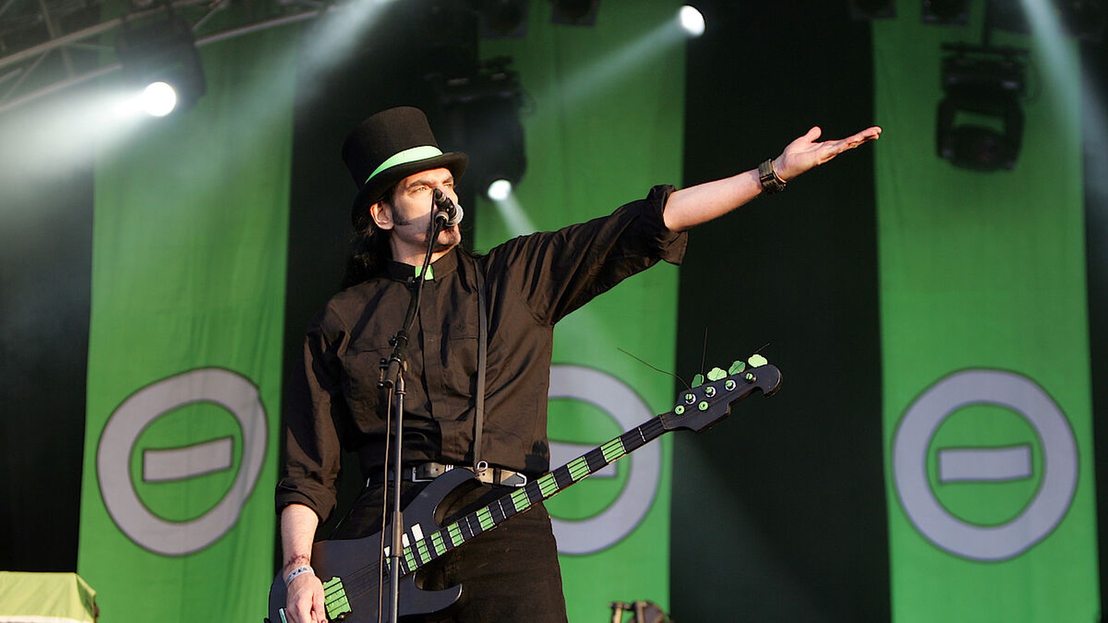 Peter Steele of Type O Negative in a top hat with a bass, arm stretched out, in front of green banners with the band logo
