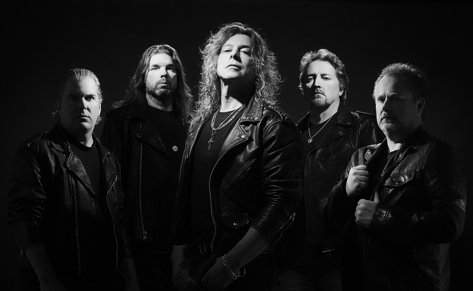 The five members of Jag Panzer in black leather, lit against a dark backdrop for a black and white studio portrait