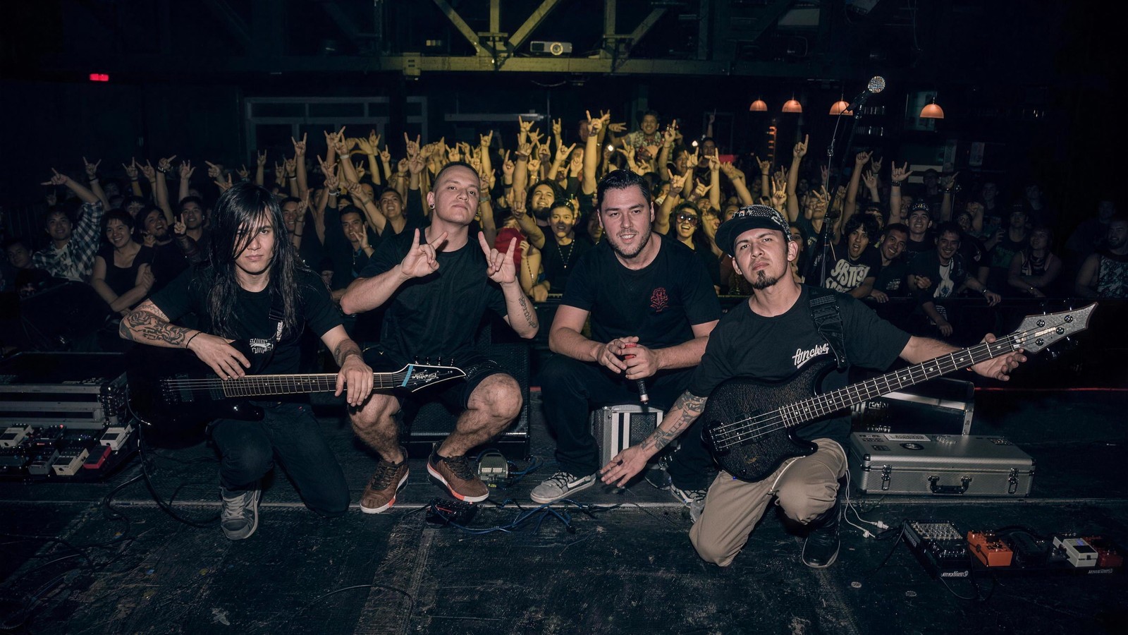Here Comes the Kraken's four members kneeling on the stage floor in front of a crowd with arms and horn signs raised, at the C3 Stage in Guadalajara, Mexico