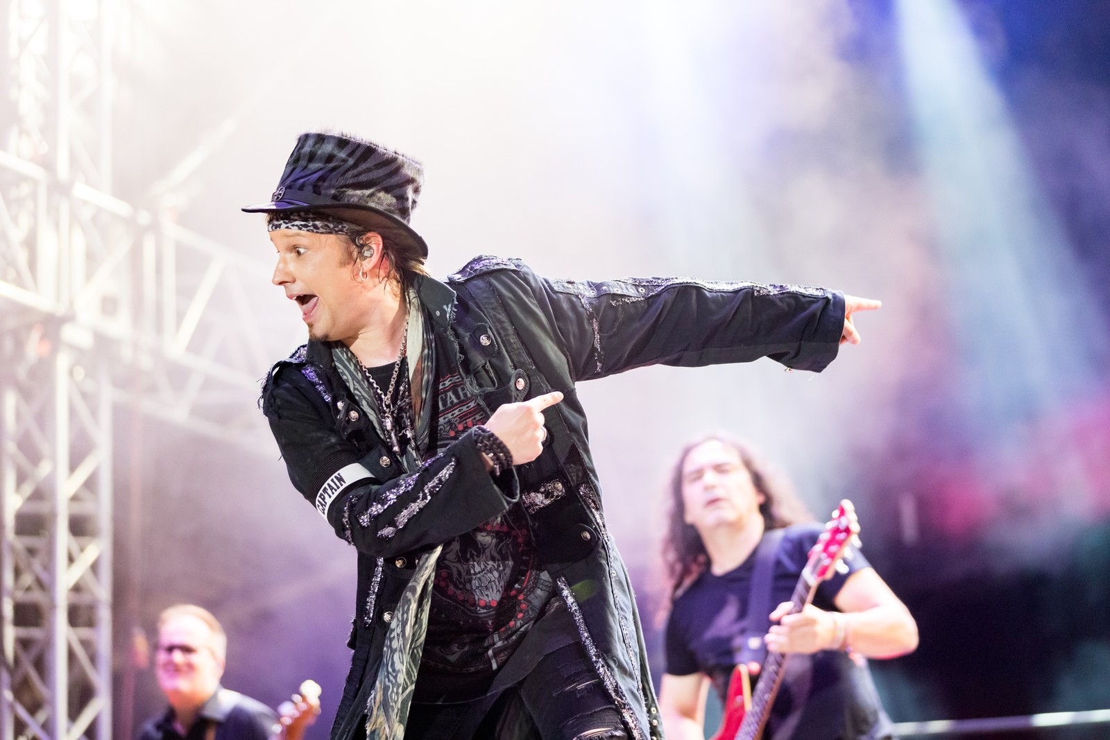 Avantasia at Wacken Open Air 2022: Tobias Sammet in a top hat and long dark coat points sharply across the stage, mouth open, with a guitarist playing behind him on the right.