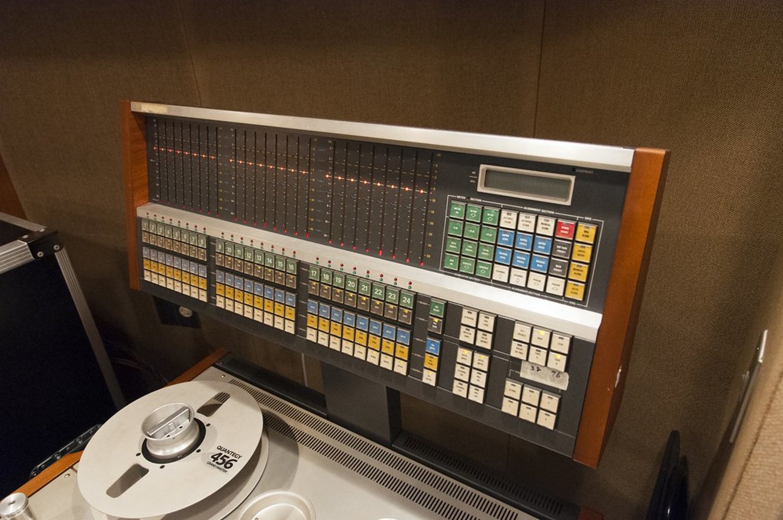 The meter bridge of a Studer two inch tape machine with a loaded reel below it, the channel meters lit