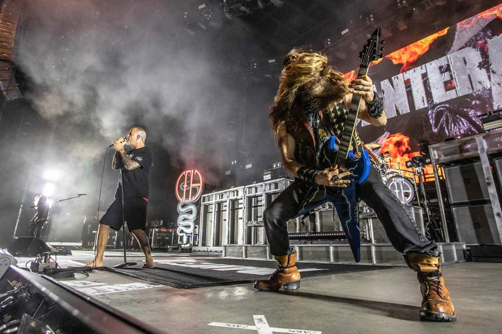 Phil Anselmo singing barefoot at the microphone while the guitarist leans into a solo in the foreground, the band name burning on the screen behind them