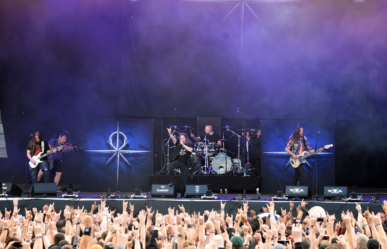 Stratovarius on the Wacken Open Air stage in 2022: the singer throws the horns at centre, a guitarist and a bassist flank the drum riser, and a crowd of raised hands fills the foreground.