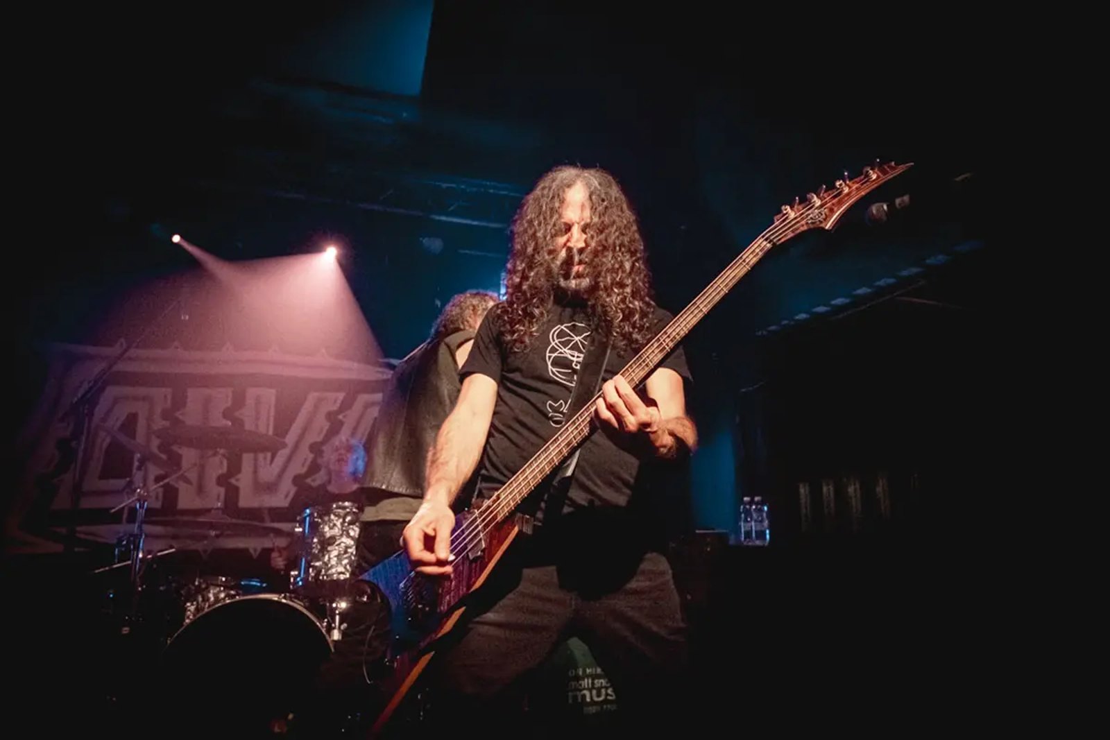The bassist of Voivod on stage at the Thekla in Bristol in June 2026, the band logo lit behind him