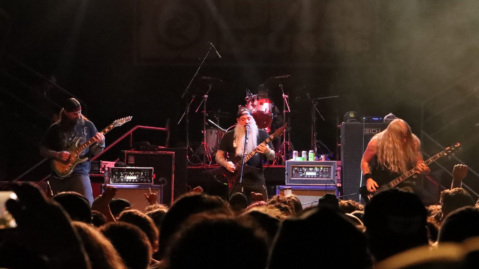 Eyehategod playing a club stage, three guitarists and the singer lit in red, the crowd filling the foreground